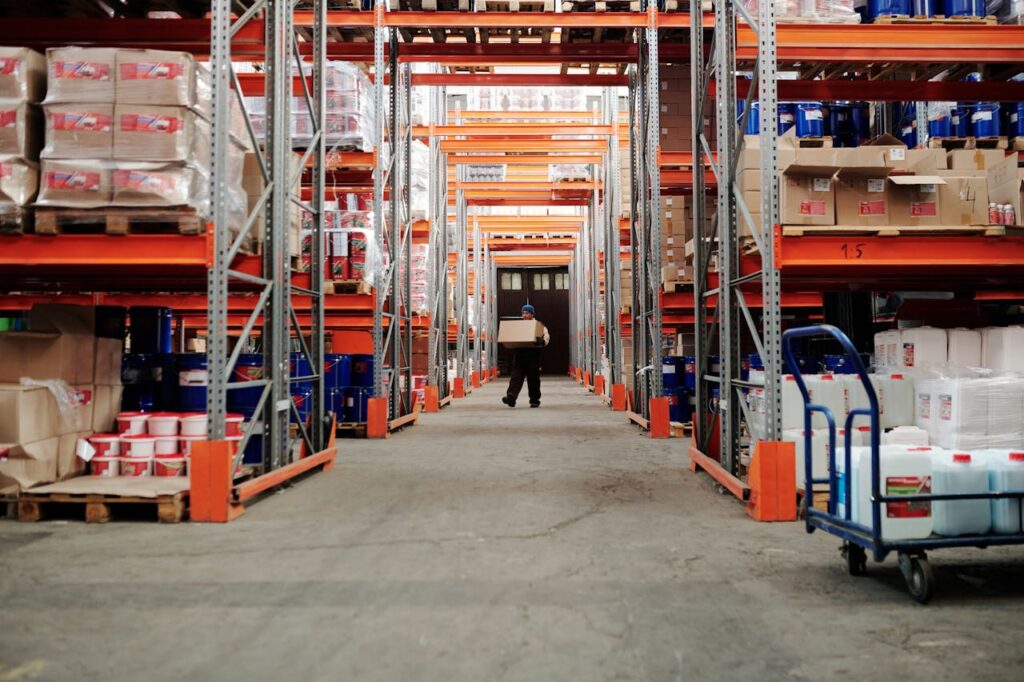 A worker carrying a box in a well-organized warehouse storage aisle.